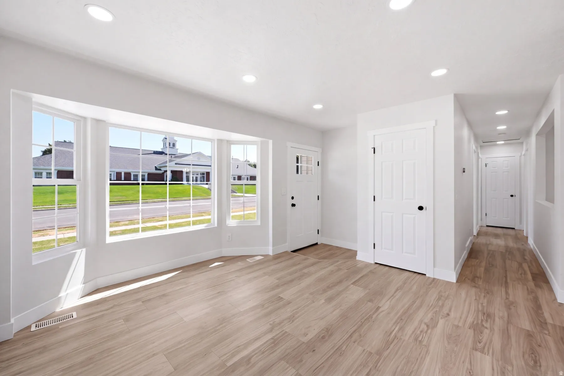 Spacious room featuring a bay window, wood-finish flooring, recessed lighting, and white trim