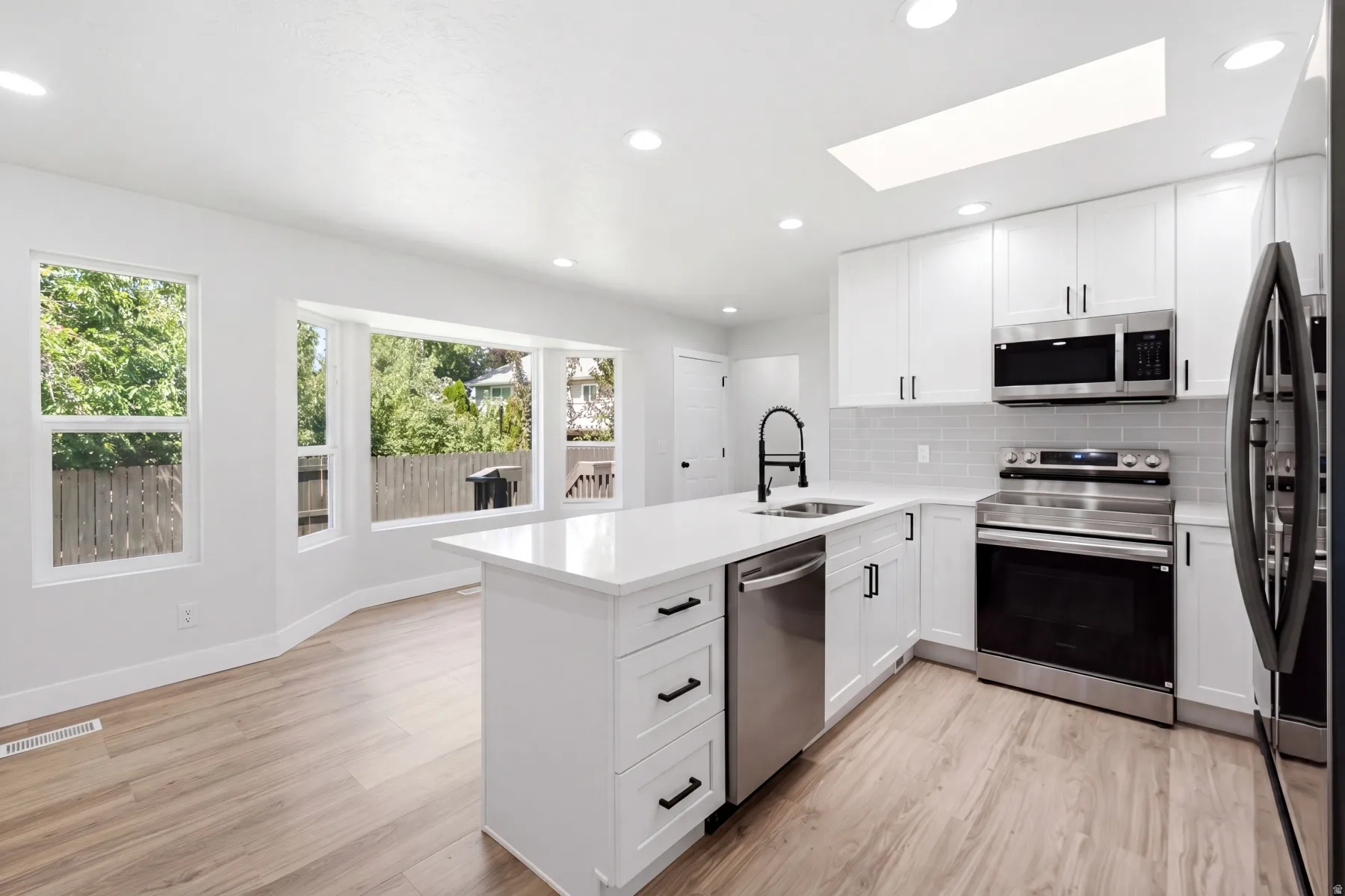 Modern kitchen featuring an island with a stainless steel sink and matte black faucet, stainless steel appliances, white cabinetry, and a subway tile backsplash