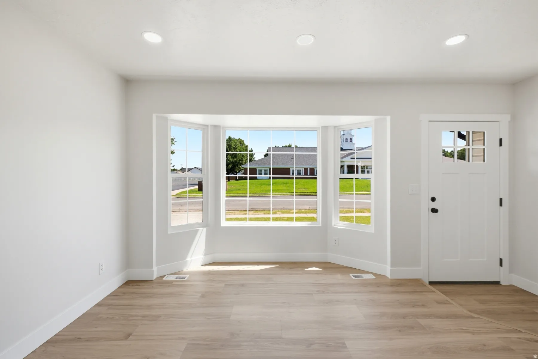 Entryway featuring a bay window, wood-finish flooring, white walls, recessed lighting, and a white paneled door with window accents