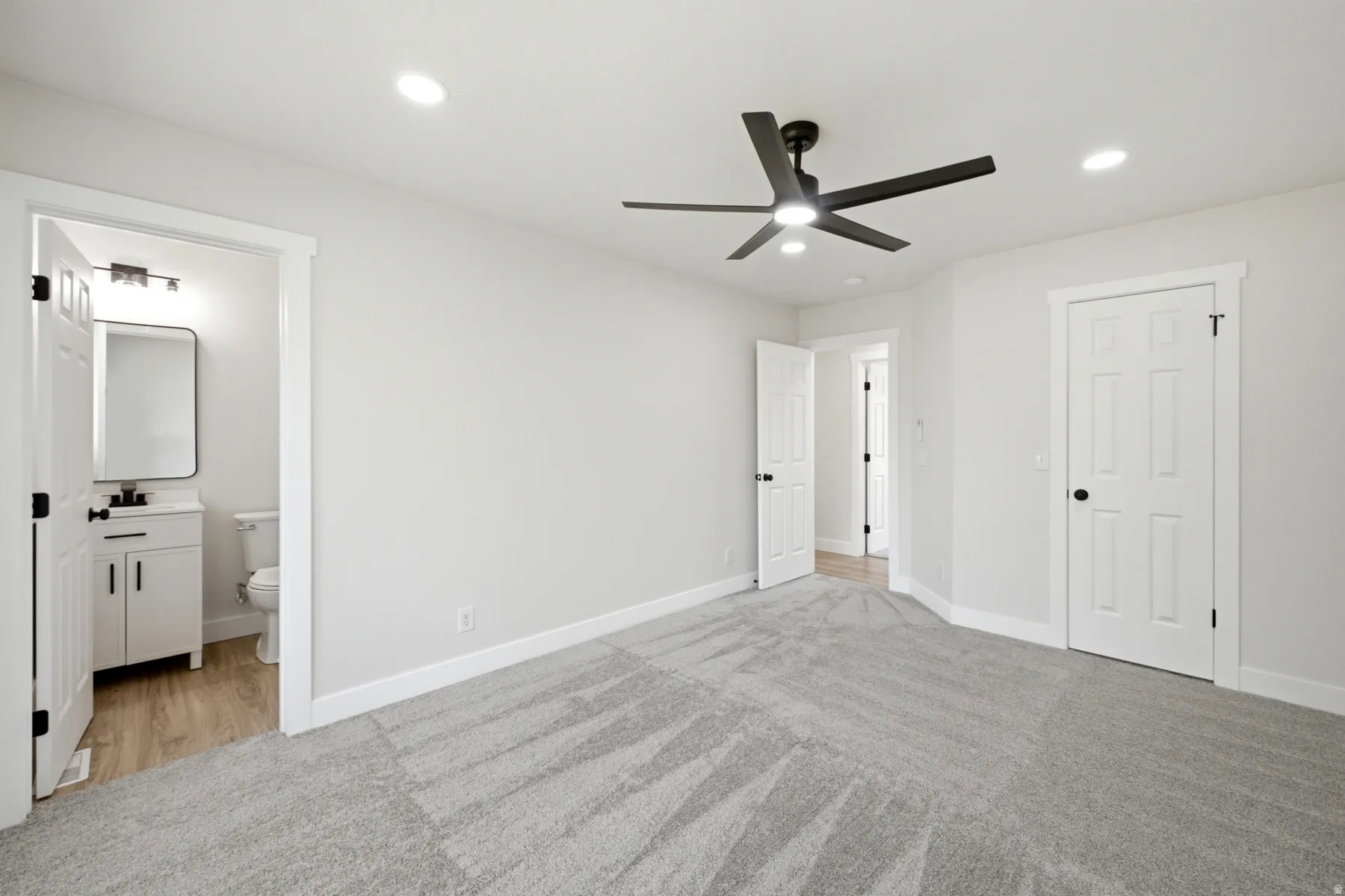 Spacious room featuring light gray carpet, recessed lighting, and a modern black ceiling fan