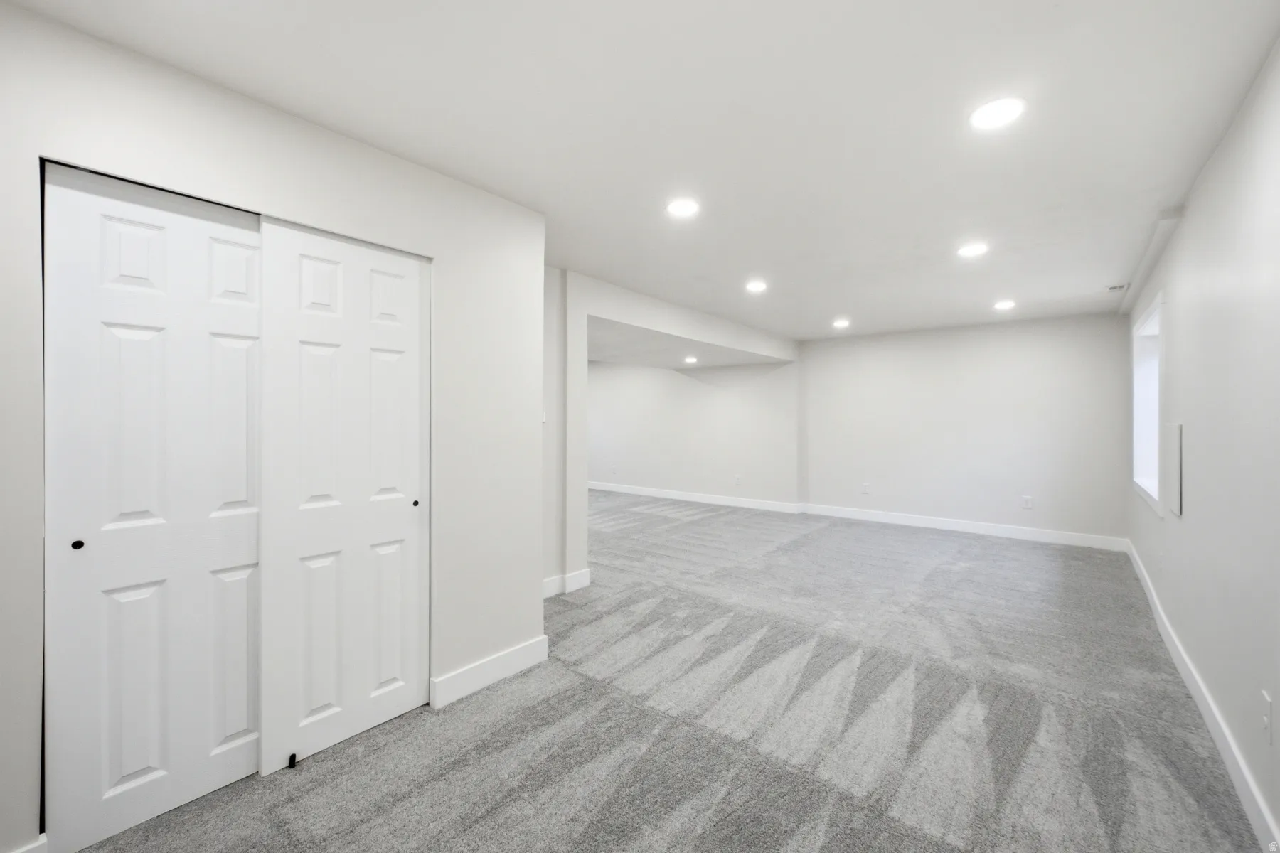 Finished lower-level space featuring recessed lighting, light gray walls, patterned gray carpeting, and white trim