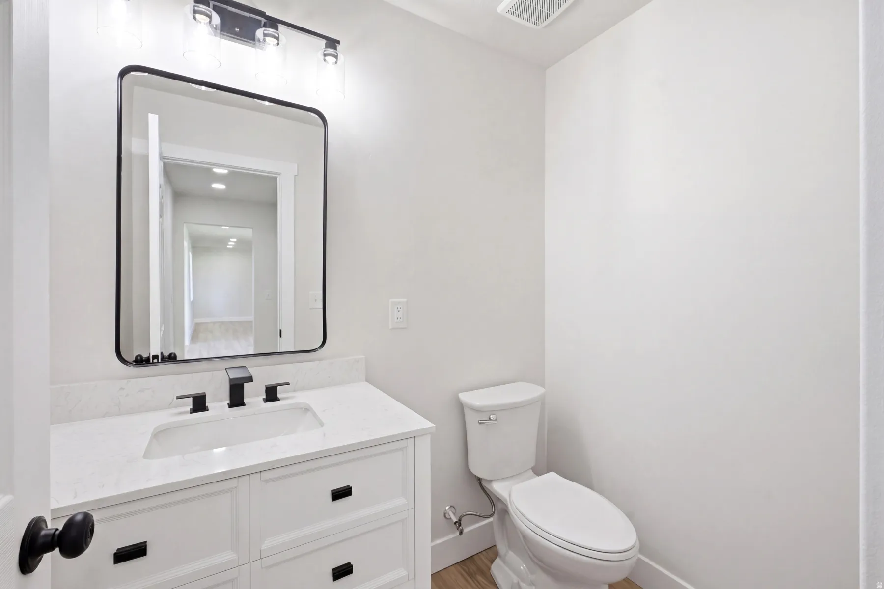 Powder room featuring a white vanity with paneling and black hardware, a rectangular undermount sink, and a light-toned countertop