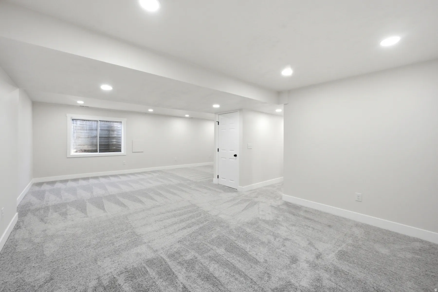 Spacious room featuring patterned carpet flooring, recessed lighting, white trim, a single window, and a white interior door