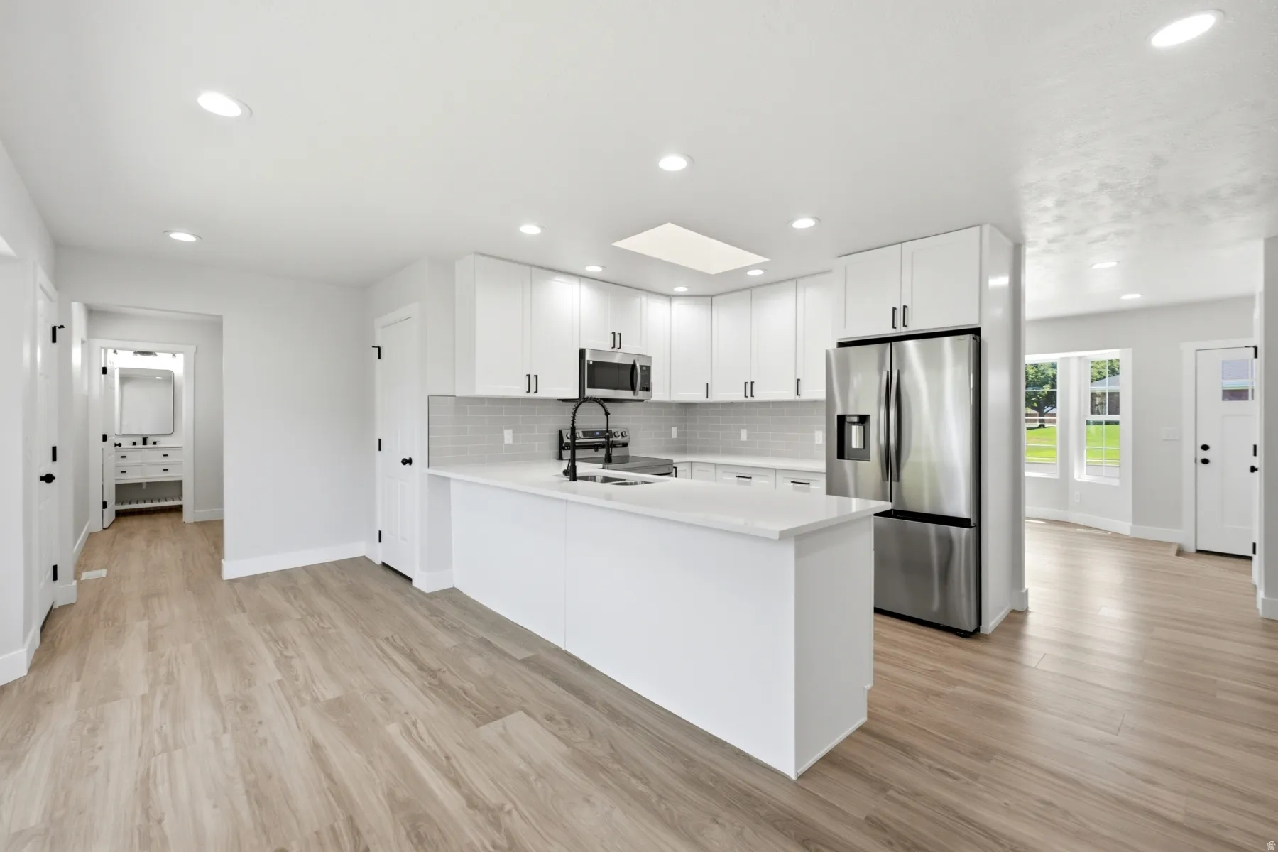 Modern kitchen featuring white cabinetry, stainless steel appliances, a white island, and a skylight