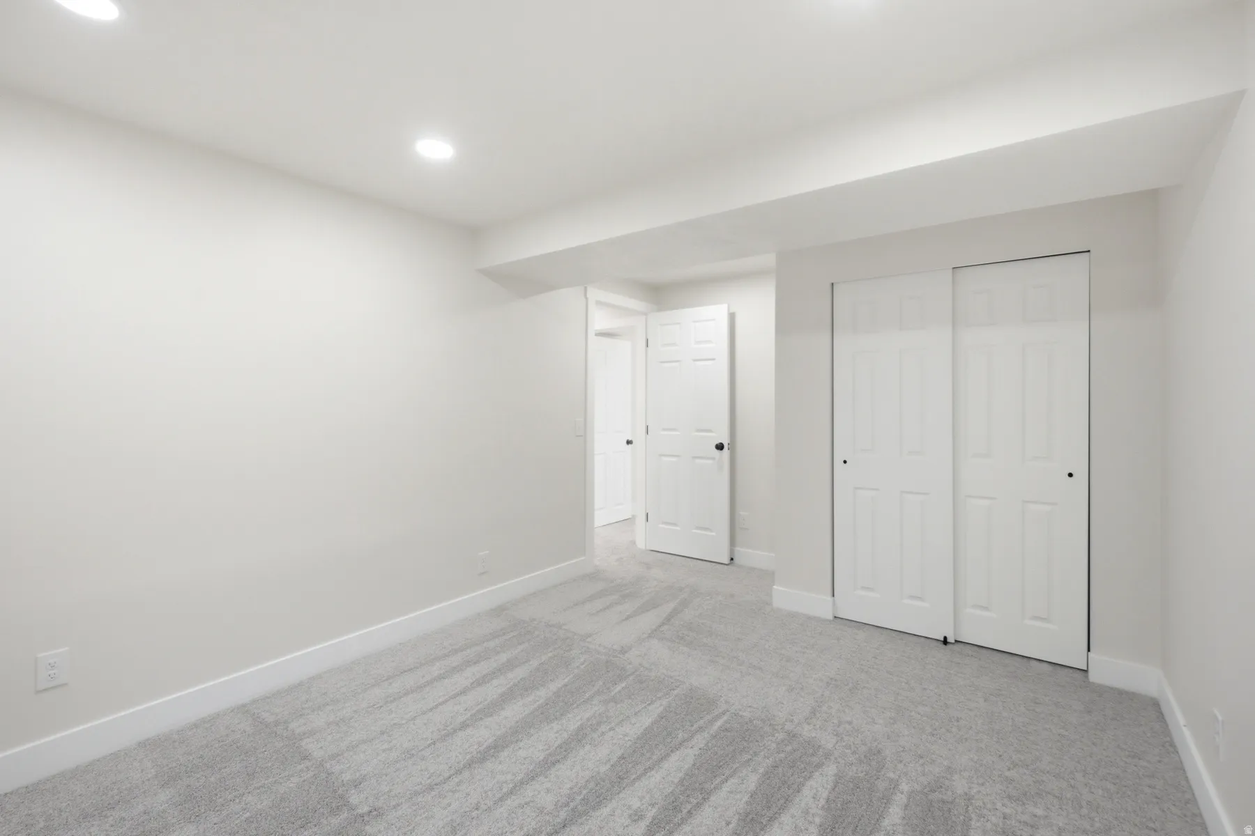 Neutral wall paint, recessed lighting, and light gray patterned carpeting