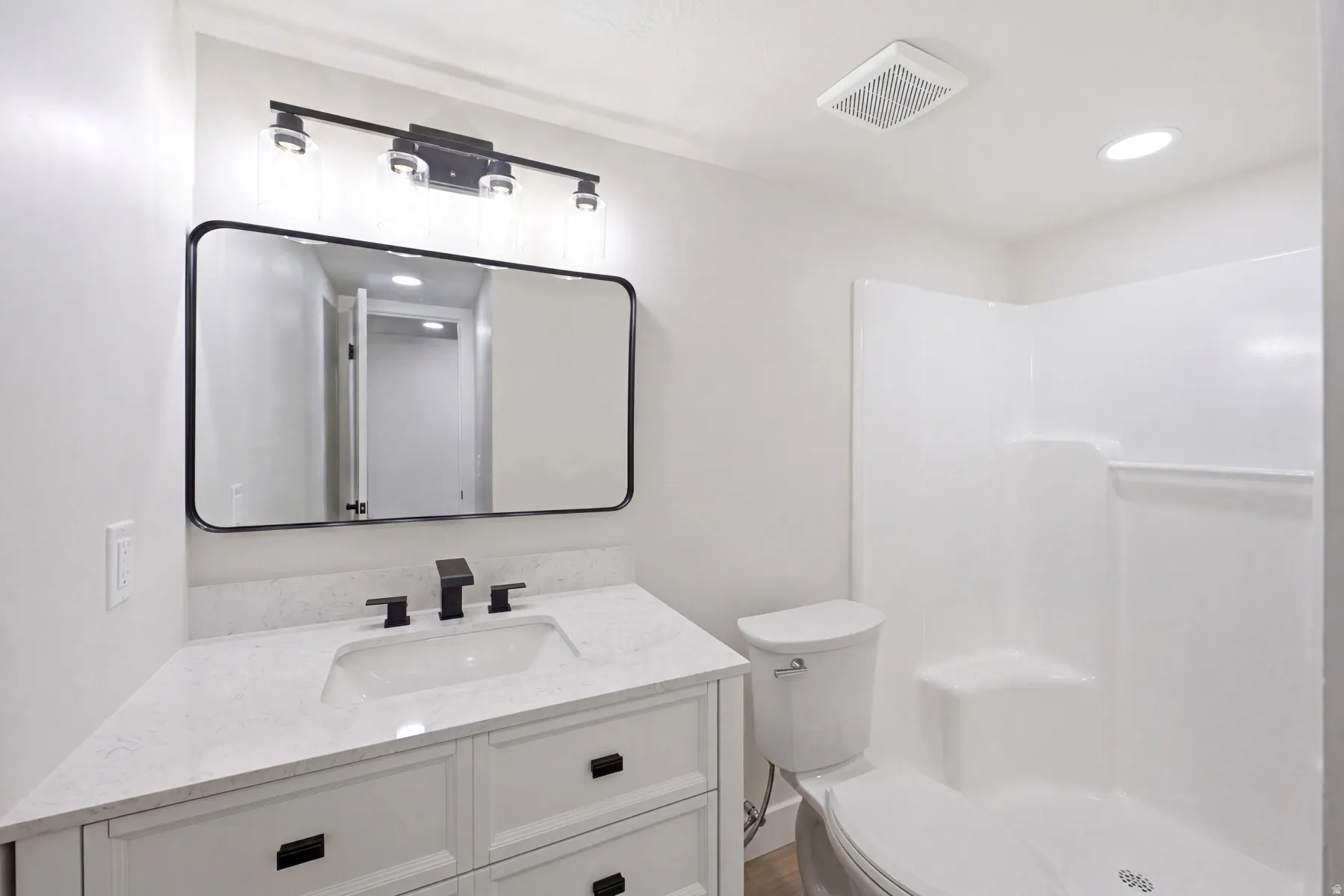 Contemporary bathroom featuring a white vanity with integrated sink, a dark-framed rectangular mirror, matte black fixtures, and a white shower/tub combination