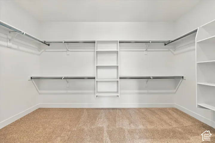 Walk-in closet featuring tiered white shelving, built-in organizers, dual-level metal hanging rods, and neutral carpeting