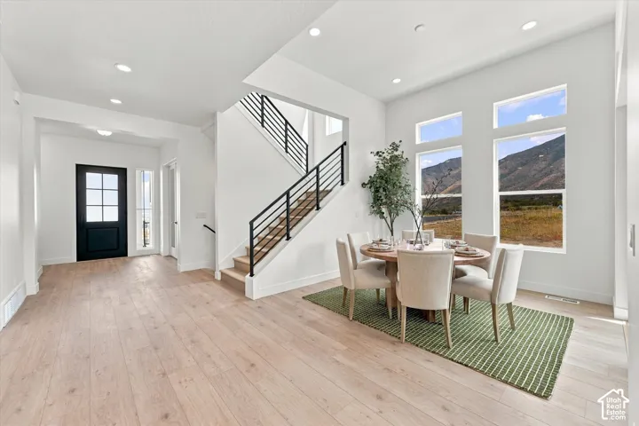 Open-concept interior featuring wood-finish flooring, staircase with matte black metal railings, recessed lighting, and expansive windows with mountain scenery