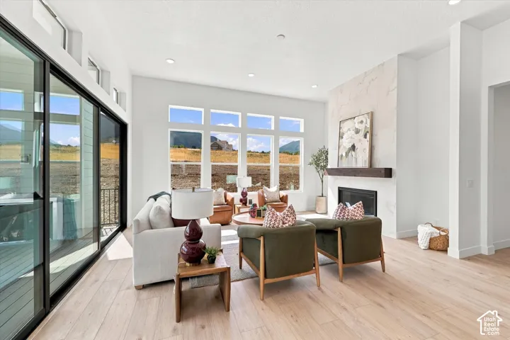 Living area featuring light-toned wood-finish flooring, a full-height stone-clad fireplace with a prominent timber mantel, oversized windows, and expansive sliding glass doors