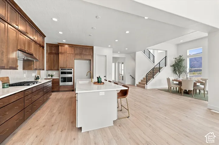 Kitchen featuring custom wood cabinetry, central island with quartz countertop, stainless steel double wall oven, and wood-finish flooring throughout