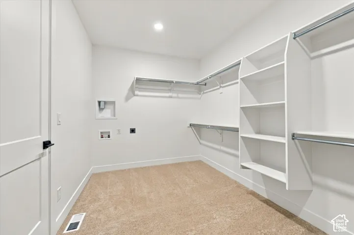 Walk-in closet featuring neutral carpeting, white built-in shelving, metal garment rods, and laundry utility hookups