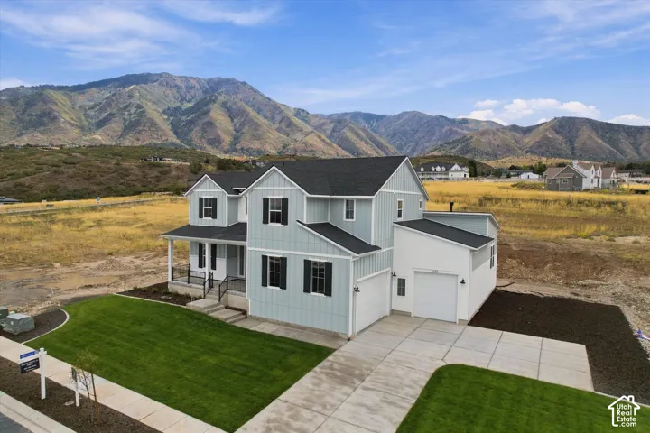 Two-story residence featuring vertical board-and-batten siding, a covered front porch with iron railings, a three-car garage, and concrete driveway, set against a prominent mountain backdrop