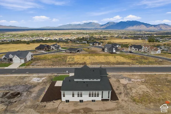 Multi-level residence featuring a dark shingle roof, light-toned exterior siding, multiple windows, and a foundation with lower-level egress windows, set against a backdrop of mountain scenery
