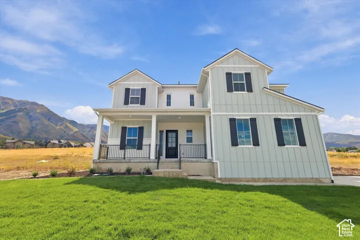 Two-story exterior featuring vertical siding, dark shutters, a covered front porch with metal railing, and a mountainous backdrop