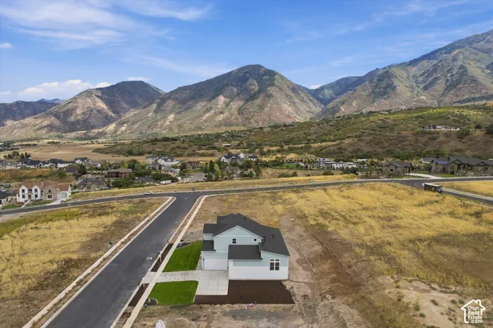 Aerial perspective of a multi-level residence featuring a multi-pitched roof, horizontal siding, attached garage, concrete driveway, and mountain backdrop