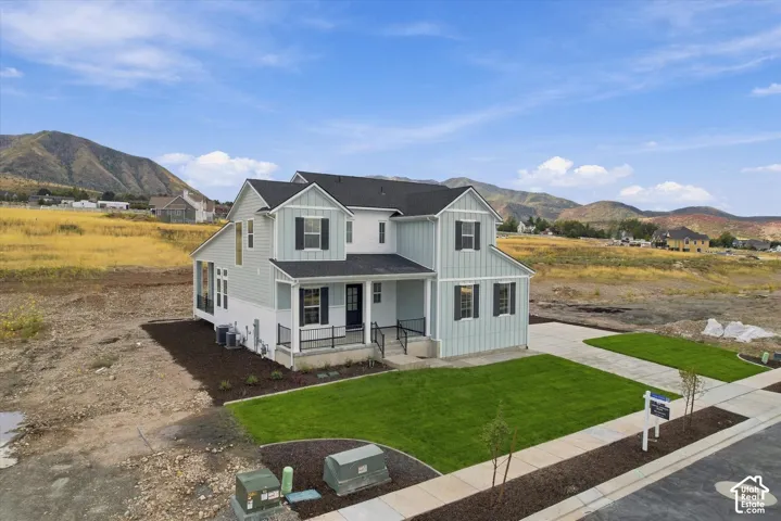 Two-story residence featuring vertical siding, a covered front porch with metal railing, an attached concrete driveway, and a mountain backdrop