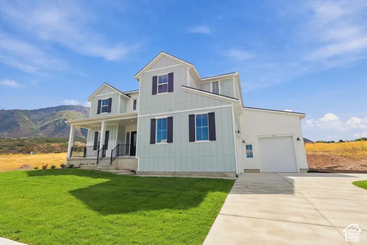 Two-story exterior featuring board-and-batten siding, a covered front porch with metal railings, an attached single-car garage, a concrete driveway, and mountain scenery