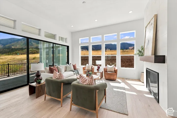 Living area featuring floor-to-ceiling windows, mountain scenery, light-toned wood-finish flooring, recessed lighting, and a fireplace with a stone-tile surround and a floating mantel