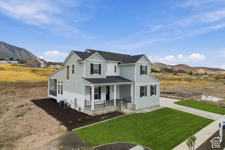 Two-story residence featuring light-toned vertical siding, a covered front porch with metal railing, a concrete driveway, and mountain scenery
