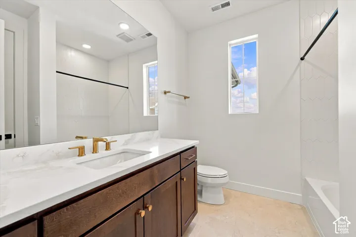 Bathroom featuring a dark wood-finish vanity with a stone countertop, an integrated rectangular sink, gold-tone hardware, and a tub-shower combination with white geometric wall tile
