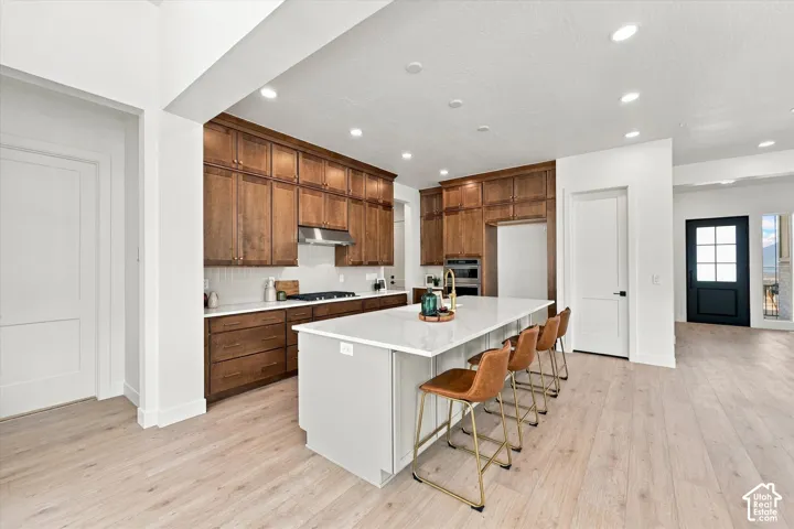 Kitchen featuring full-height wood cabinetry, stone countertops, central island, wood-finish flooring, and recessed lighting