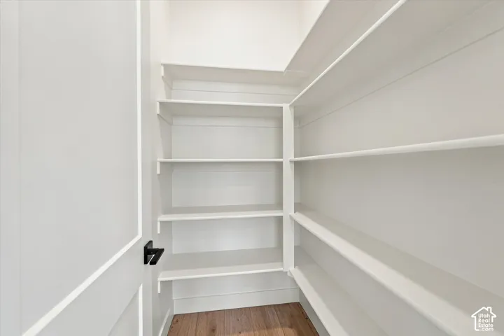 Walk-in storage space featuring custom white shelving, shiplap wall detailing, wood-finish flooring, and a matte black door handle