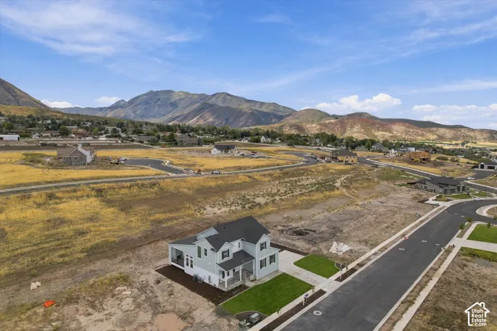 Aerial perspective of a two-story residence with a multi-gabled roofline and an attached covered patio, situated on a lot with landscaped turf and direct mountain range scenery