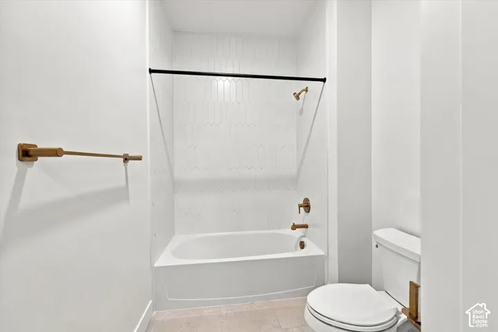Bathtub with white elongated picket tile surround, metallic bronze hardware, matte black shower rod, and light-toned tile flooring