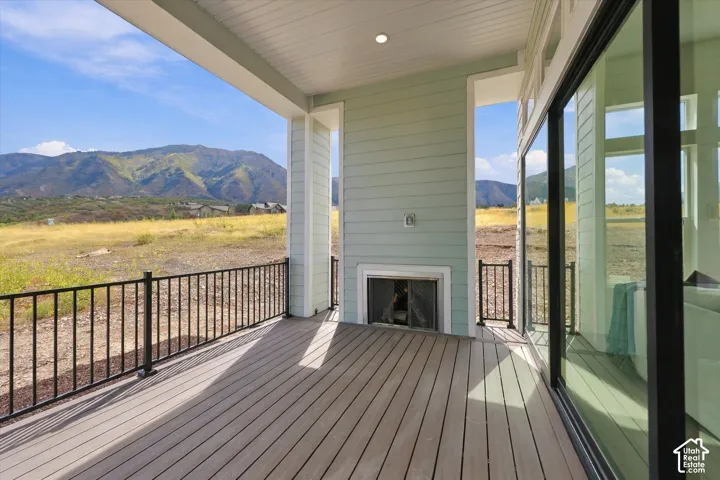 Covered patio featuring composite decking, a built-in outdoor fireplace, black metal railing, and recessed ceiling lighting