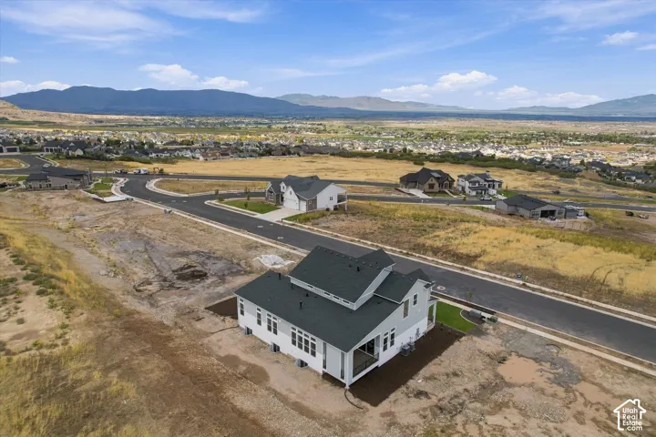 Aerial perspective featuring a two-story residence with a pitched shingle roof, integrated covered patio, and mountain horizon backdrop