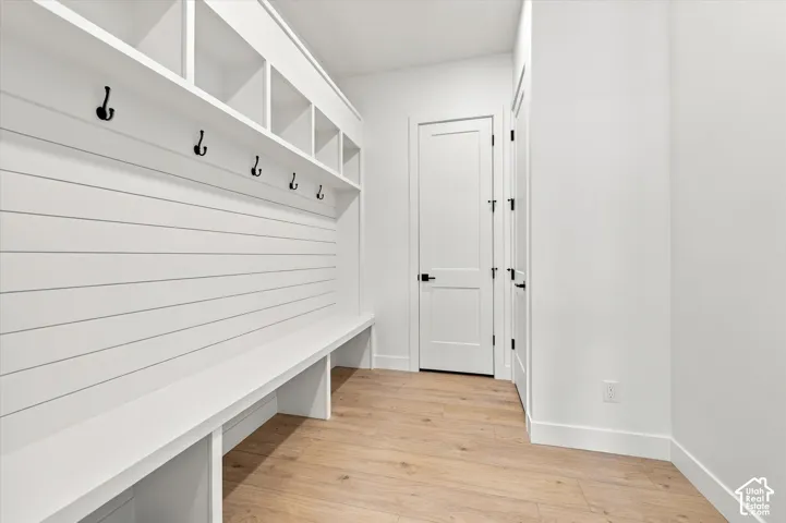 Built-in white storage cabinetry featuring shiplap detailing, overhead cubbies, and integrated hooks, accented by matte black hardware and wood-finish flooring