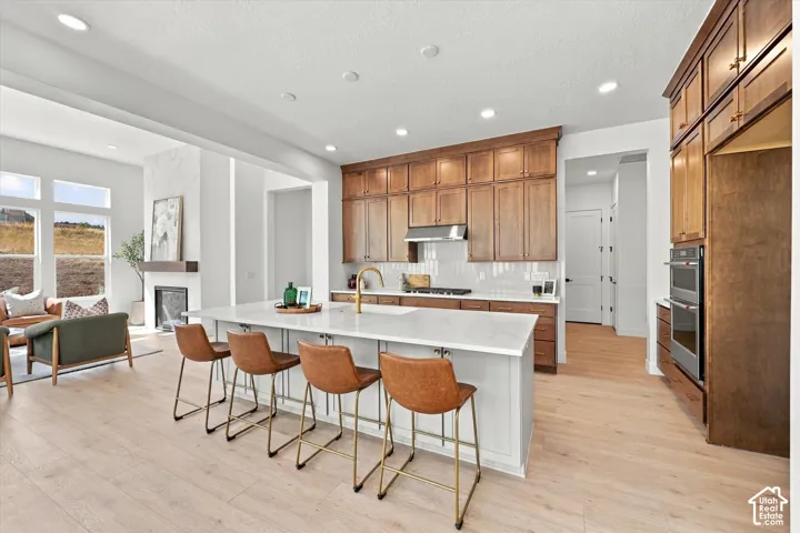 Kitchen featuring wood cabinetry, a central island with a quartz countertop, built-in double ovens, light-toned wood-finish flooring, and recessed ceiling lighting