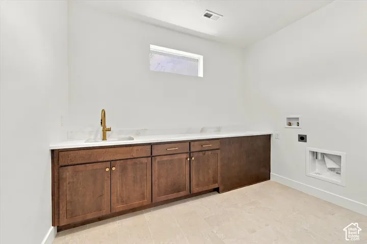 Utility space featuring custom wood cabinetry, integrated sink with gold-tone faucet, light-toned stone-finish countertop, and tile flooring