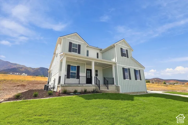 Two-story exterior featuring board-and-batten siding, a covered front porch, dark window shutters, metal railings, and a concrete foundation with a backdrop of mountainous terrain