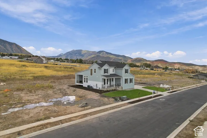 Two-story exterior featuring a light-toned siding, covered front porch, asphalt shingle roof, and mountain backdrop