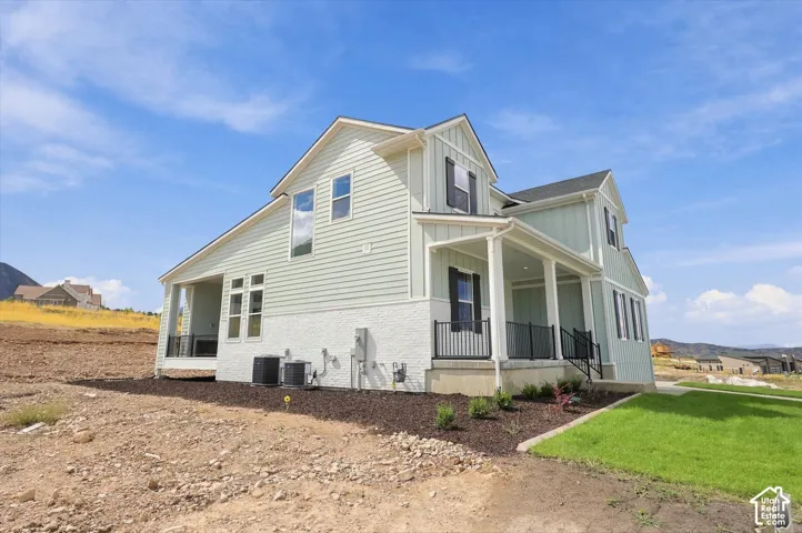 Two-story exterior featuring light green board-and-batten and horizontal siding, white painted masonry base, covered porch with metal railing, and mountain backdrop