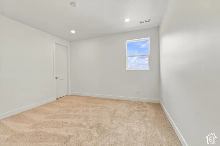 Interior space featuring neutral wall-to-wall carpeting, white walls, recessed ceiling lighting, and a solid-core interior door with black hardware