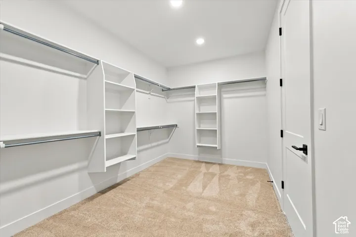 Walk-in closet featuring white built-in shelving, integrated hanging rods, wall-to-wall carpeting, and a shaker-style door with matte black hardware