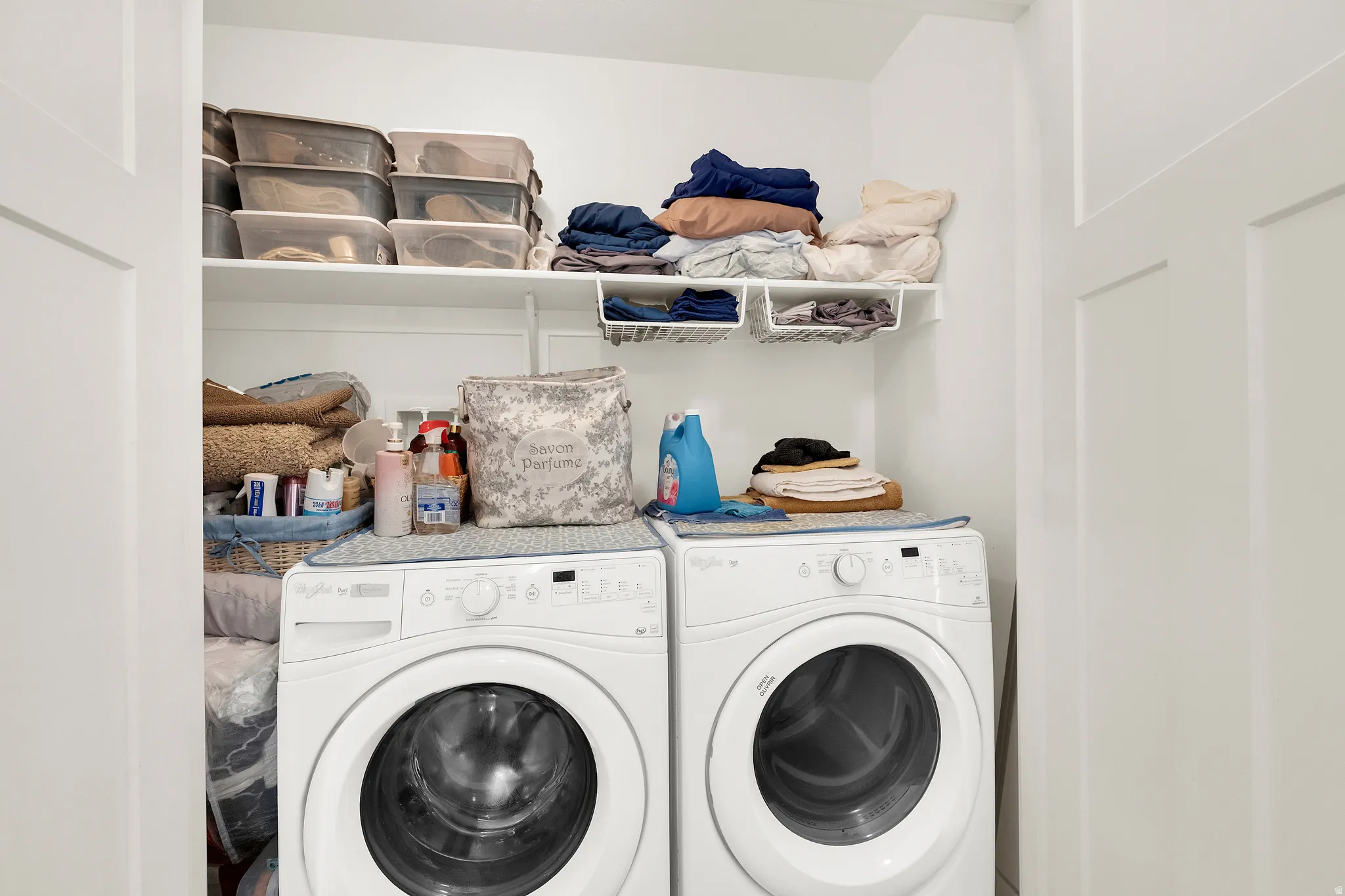 Dedicated laundry alcove featuring white bi-fold doors, two white front-loading washing machines, and integrated shelving for storage