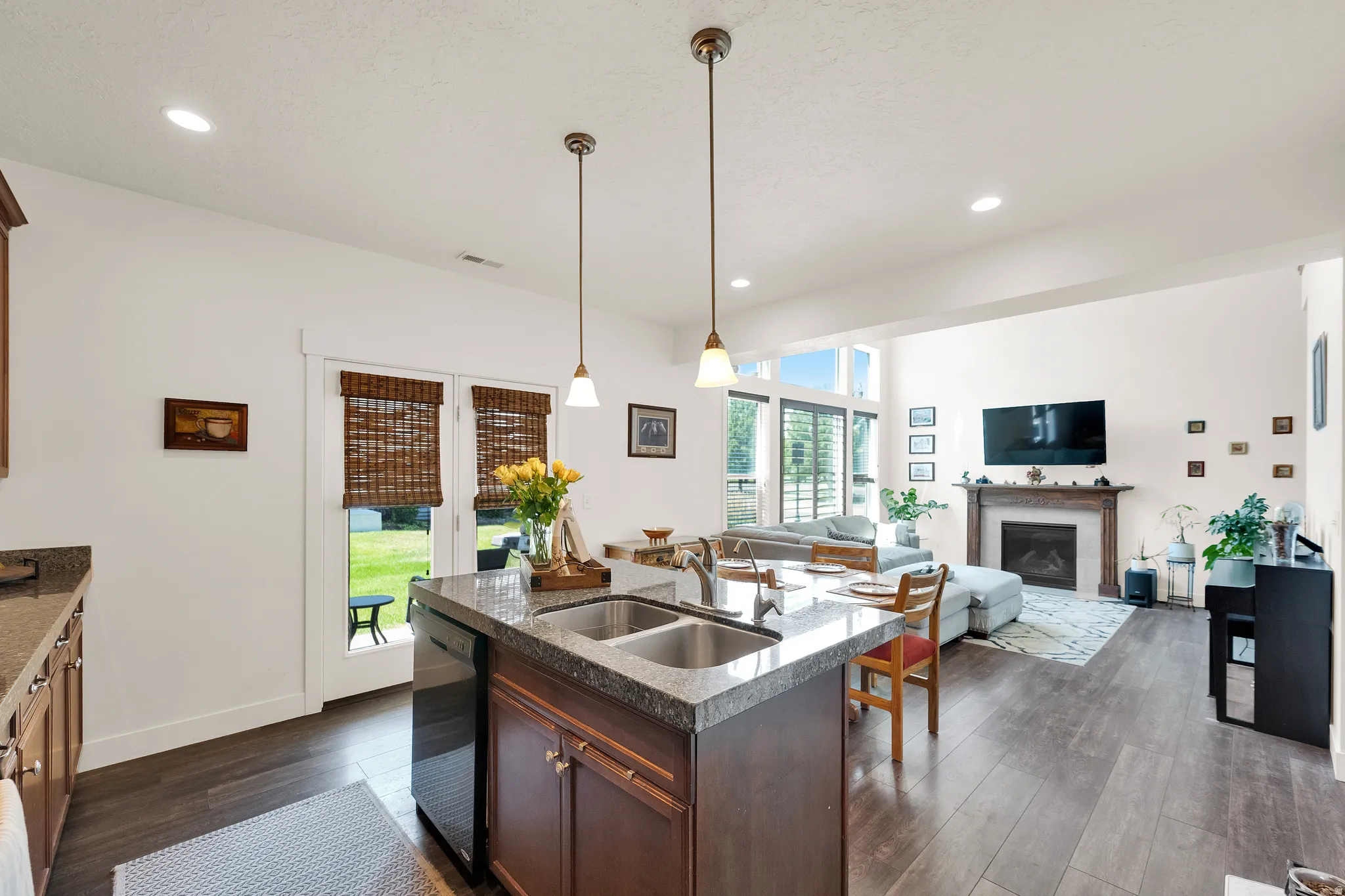 Open-concept living space featuring wood-finish flooring, a kitchen island with dual sinks and pendant lighting, and direct access to the outdoor area through double glass doors