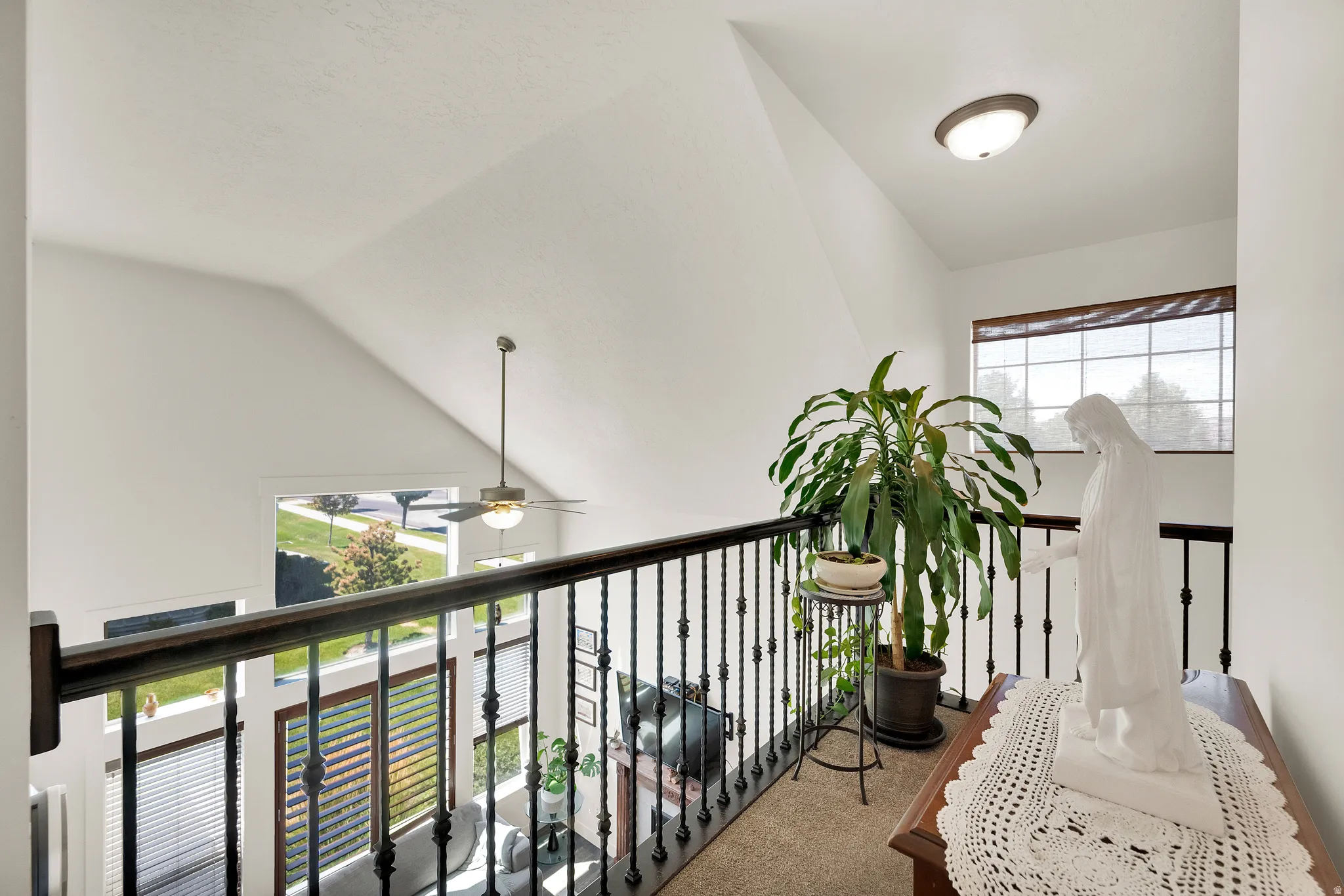 Carpeted landing with black wrought iron railing, a vaulted ceiling, and a flush mount light fixture