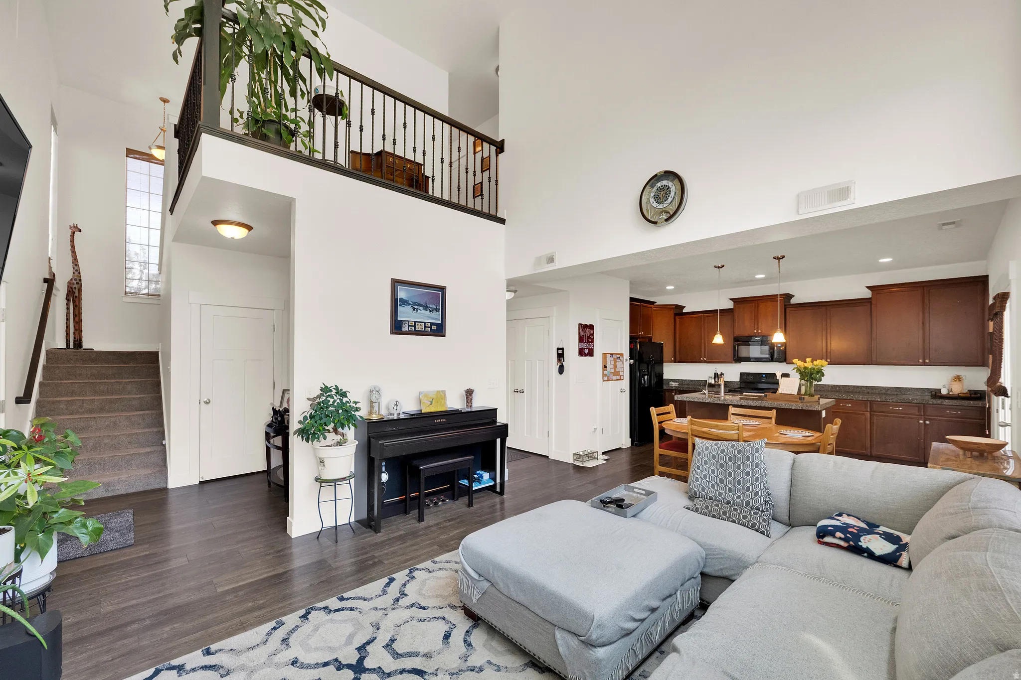 Vaulted ceilings enhance this open-concept living space, featuring wood-finish flooring, a carpeted staircase, and an upper-level balcony with black iron railings