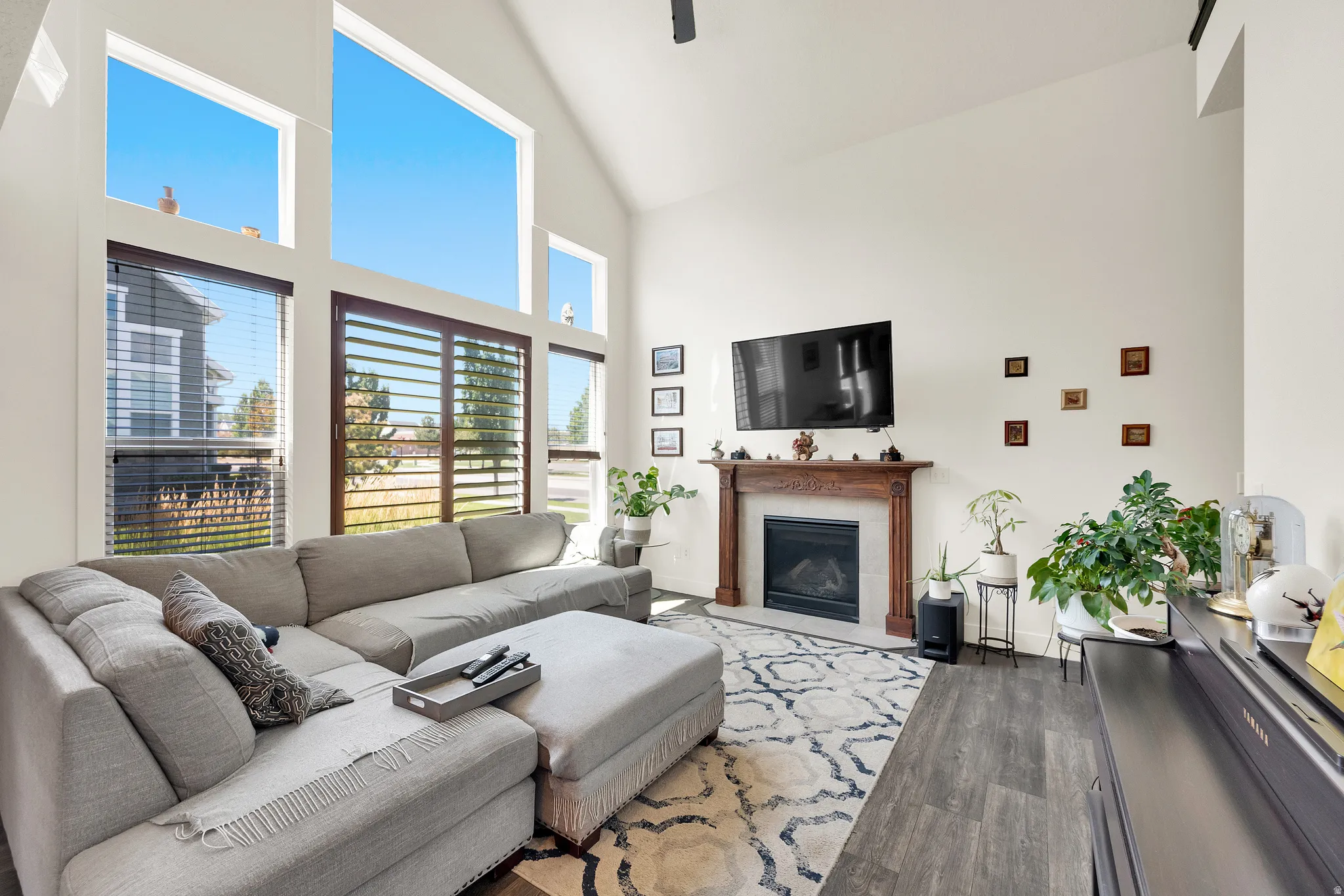 Living area featuring vaulted ceilings, floor-to-ceiling windows, wood-finish flooring, a decorative area rug, and a fireplace with a carved wood mantel