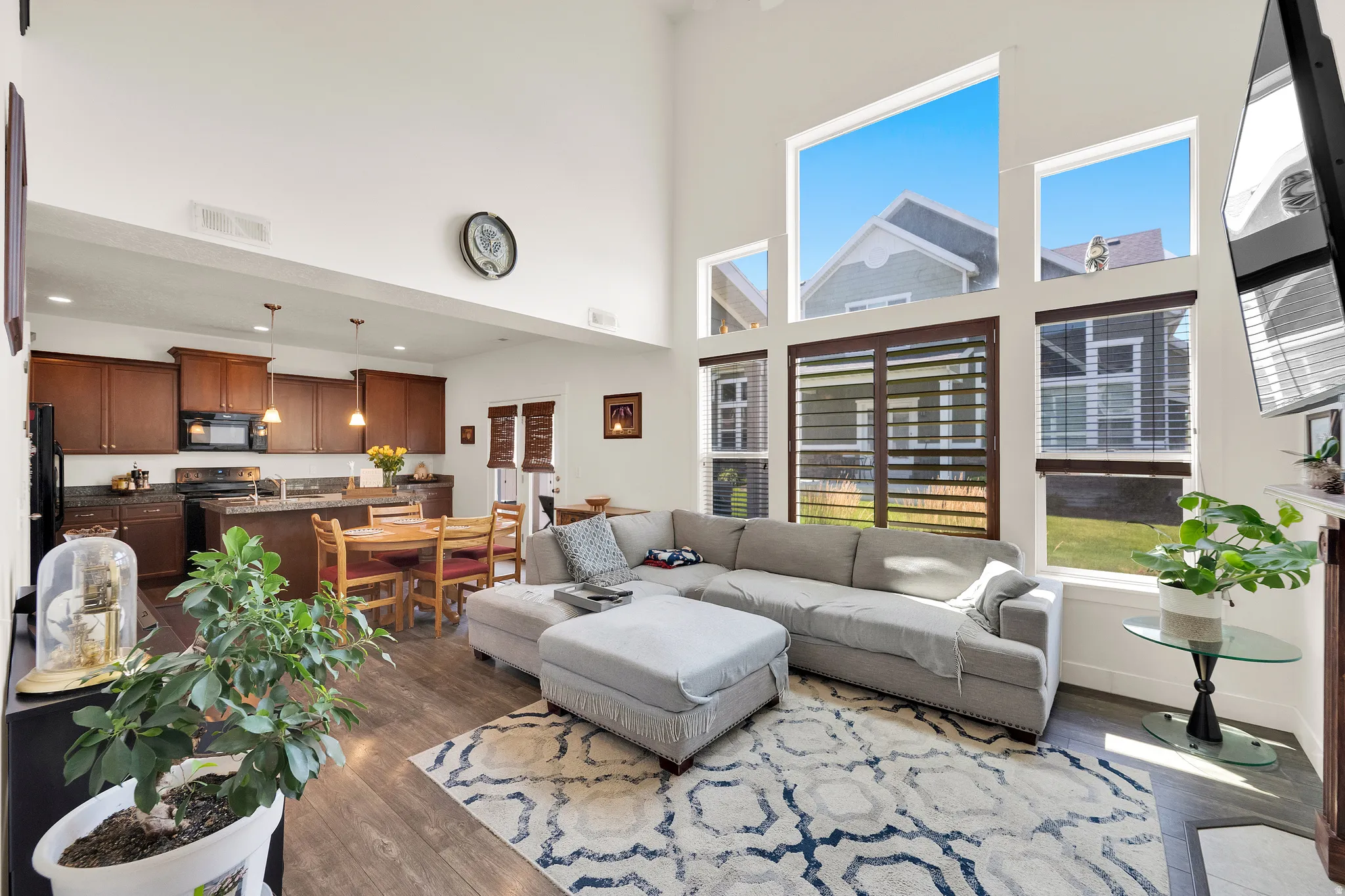 Vaulted ceiling living space featuring abundant natural light, wood-finish flooring, and an open-concept kitchen with dark wood cabinetry