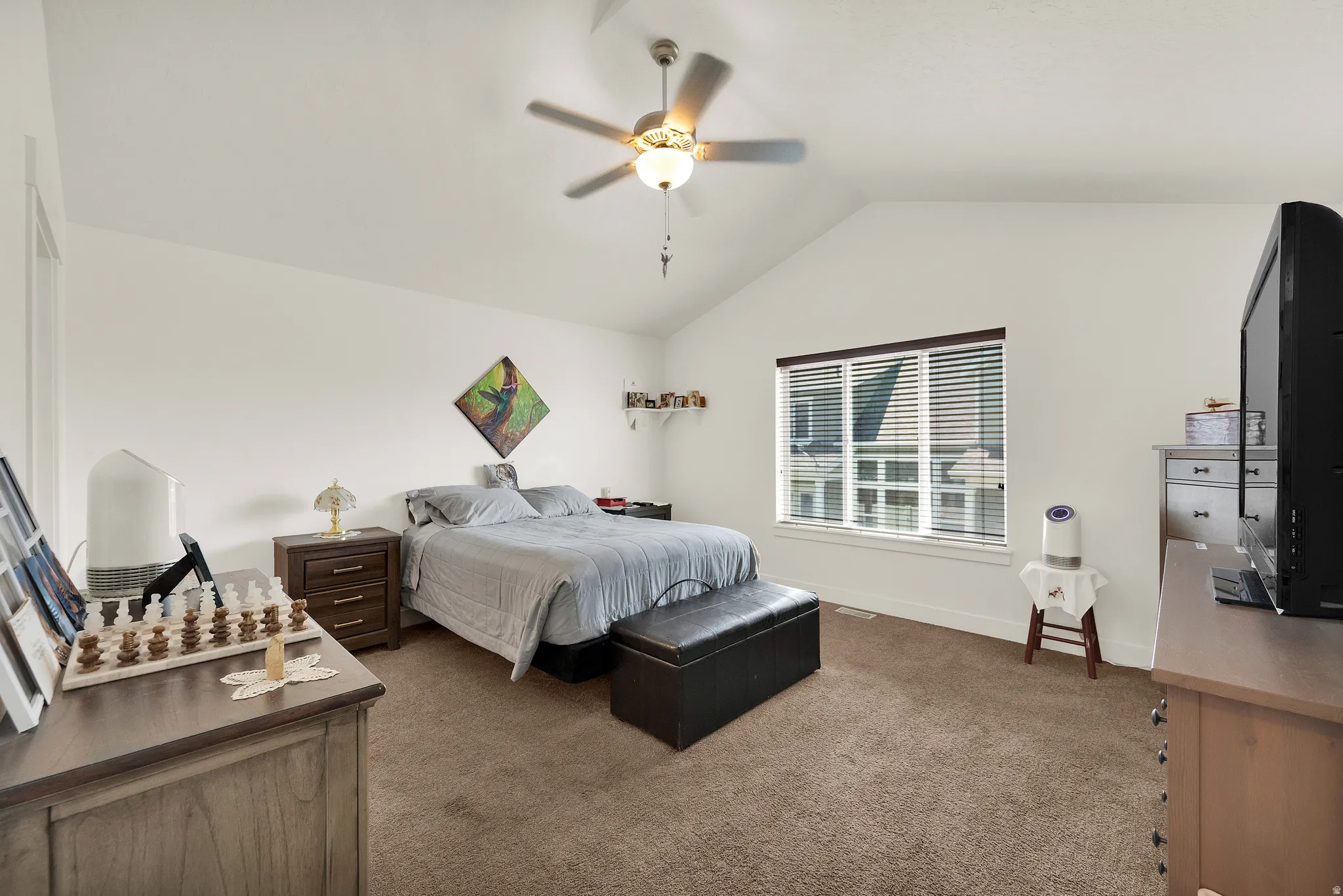 Vaulted ceilings with a ceiling fan light fixture, carpeted flooring, and a large window with blinds