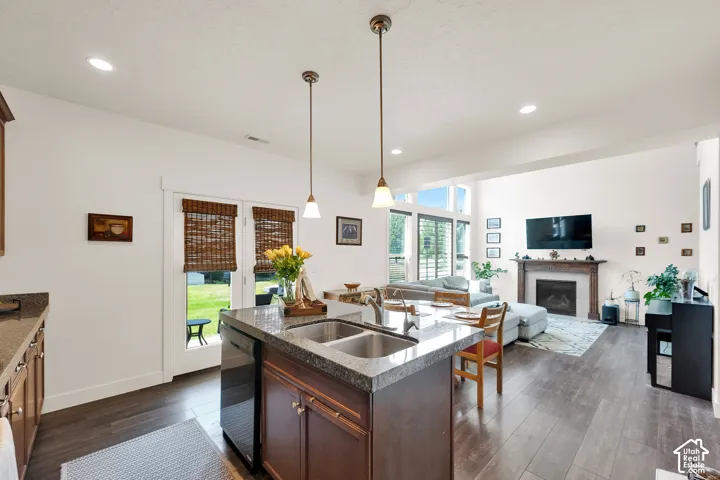 Open-concept living space featuring wood-finish flooring, a kitchen island with dual sinks and pendant lighting, and direct access to the outdoor area through double glass doors