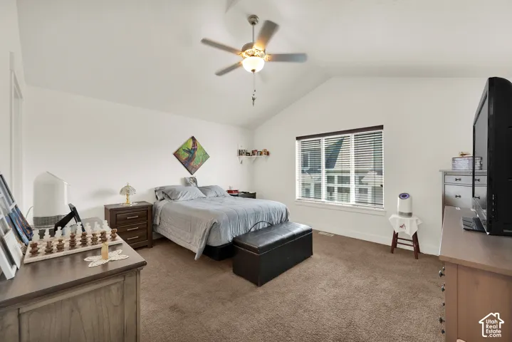 Vaulted ceilings with a ceiling fan light fixture, carpeted flooring, and a large window with blinds