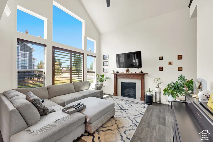 Living area featuring vaulted ceilings, floor-to-ceiling windows, wood-finish flooring, a decorative area rug, and a fireplace with a carved wood mantel