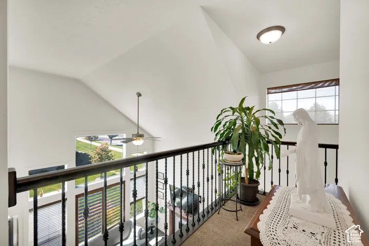 Carpeted landing with black wrought iron railing, a vaulted ceiling, and a flush mount light fixture