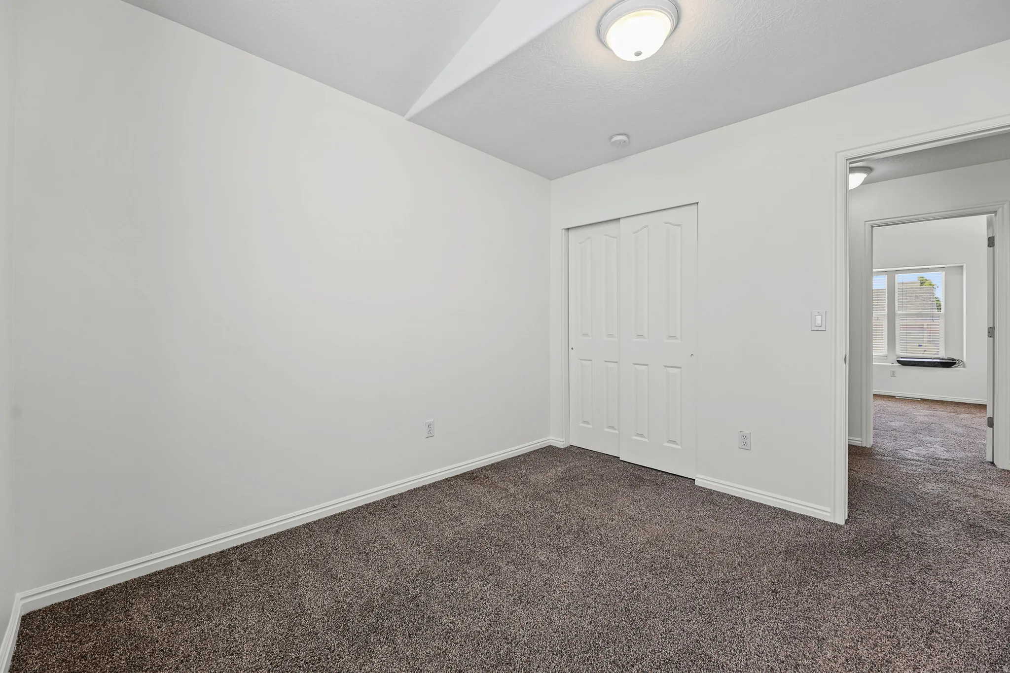 Room featuring neutral wall tones, dark gray carpet flooring, white baseboards, and a white bi-fold closet door